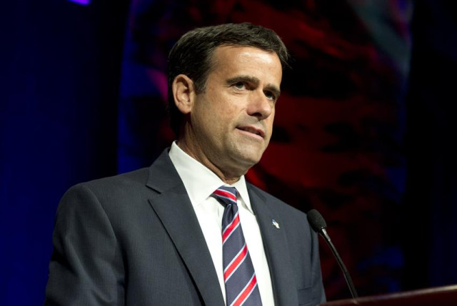 John Ratcliffe, wearing a suit and striped tie, speaks at a podium with a microphone.